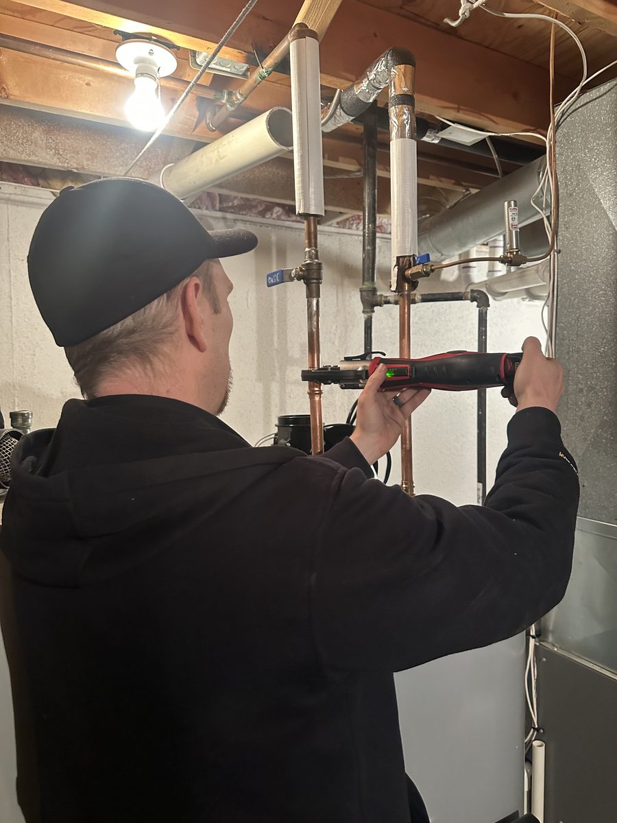 RC Heating & Cooling technician pressing overhead copper pipe during a water heater install